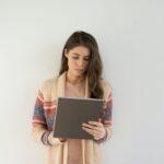 woman in beige, gray, and red sweater holding silver tablet computer