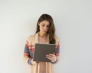 woman in beige, gray, and red sweater holding silver tablet computer