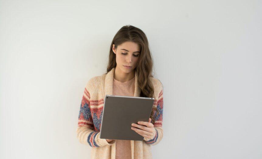 woman in beige, gray, and red sweater holding silver tablet computer