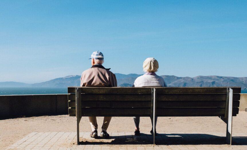 man and woman sitting on bench facing sea