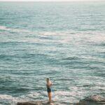 woman in white shirt and black shorts standing on sea shore during daytime