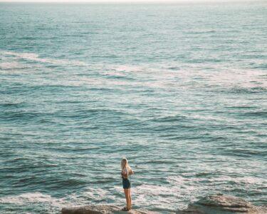 woman in white shirt and black shorts standing on sea shore during daytime