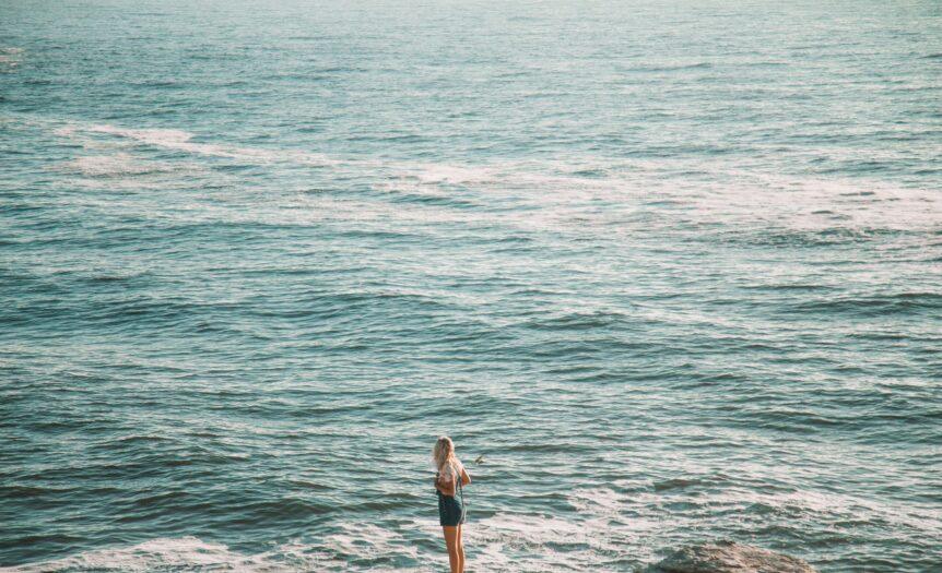 woman in white shirt and black shorts standing on sea shore during daytime
