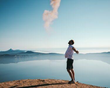 man standing on sand while spreading arms beside calm body of water