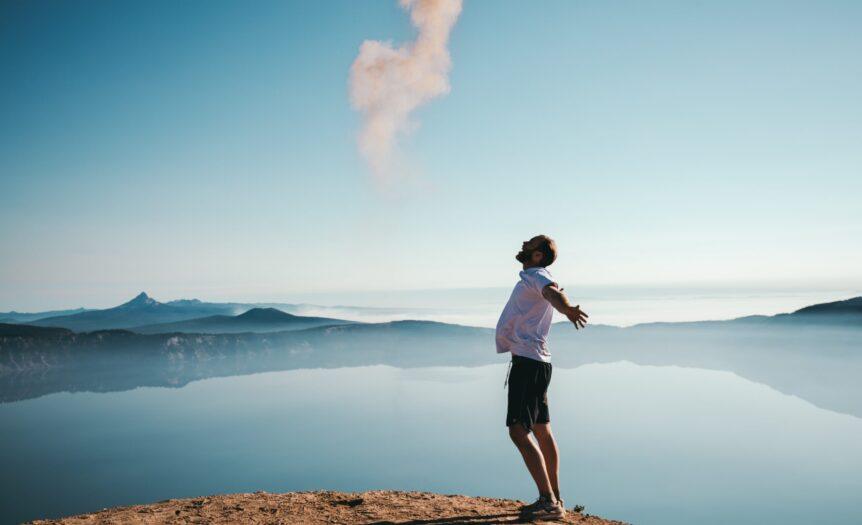 man standing on sand while spreading arms beside calm body of water