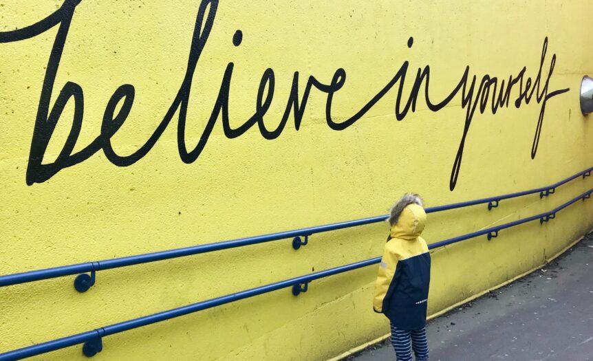 toddler looking at believe in yourself graffiti