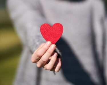 A woman presenting a red heart symbol, showcasing love and compassion.