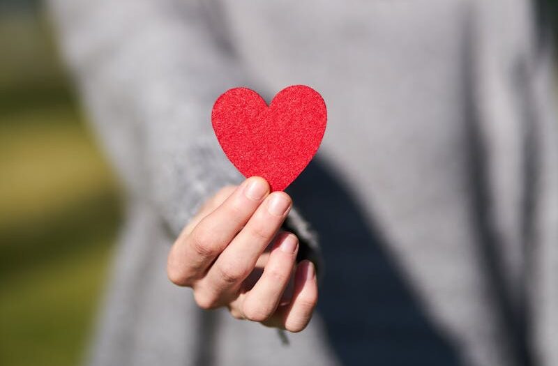 A woman presenting a red heart symbol, showcasing love and compassion.