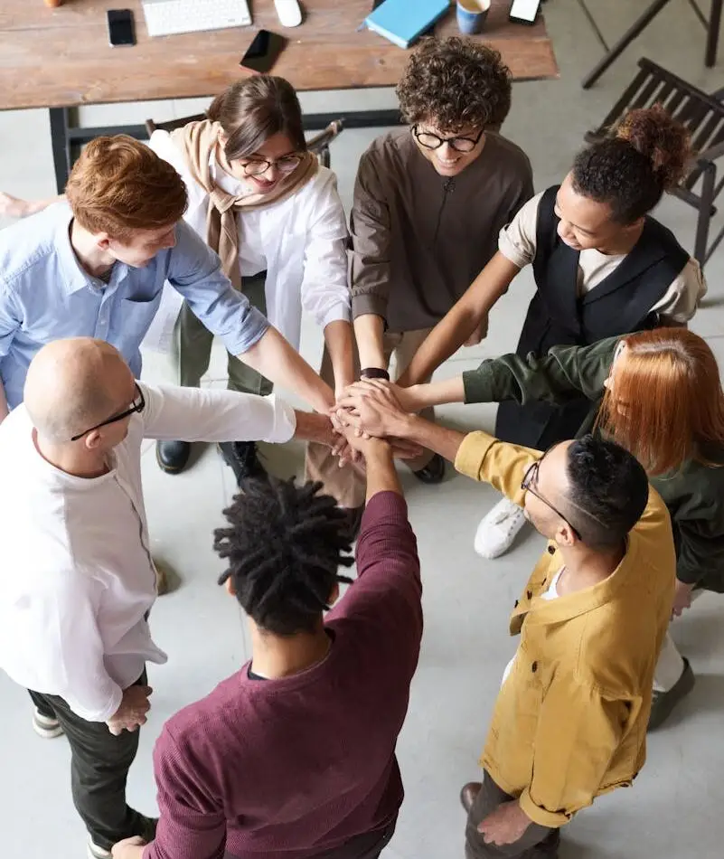 A diverse group of professionals joins hands in a team-building exercise indoors.