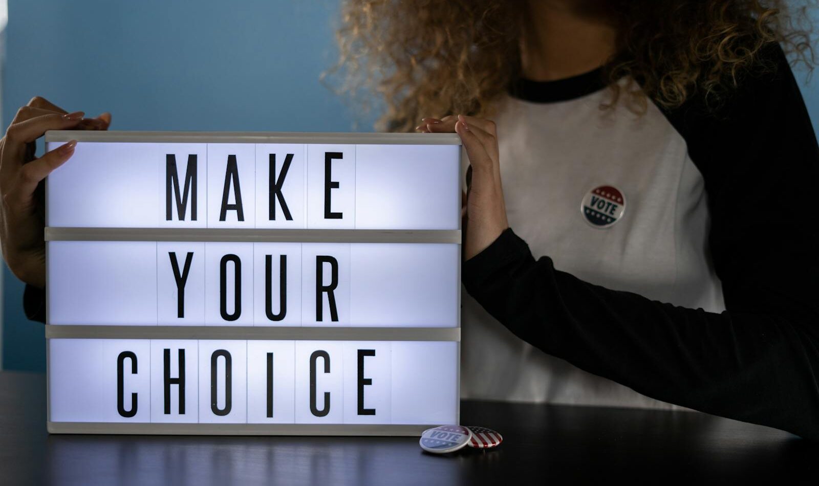 Woman holding lightbox with 'Make Your Choice' promoting civic duty and voting.