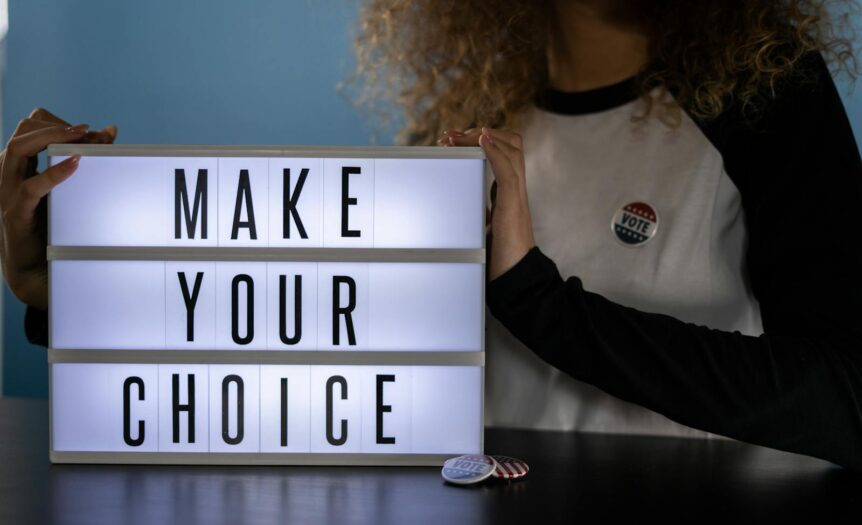 Woman holding lightbox with 'Make Your Choice' promoting civic duty and voting.