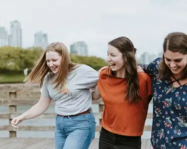 three women walking on brown wooden dock near high rise building during daytime