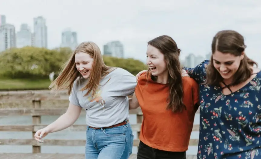 three women walking on brown wooden dock near high rise building during daytime