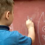 a little boy writing on a wall with a marker
