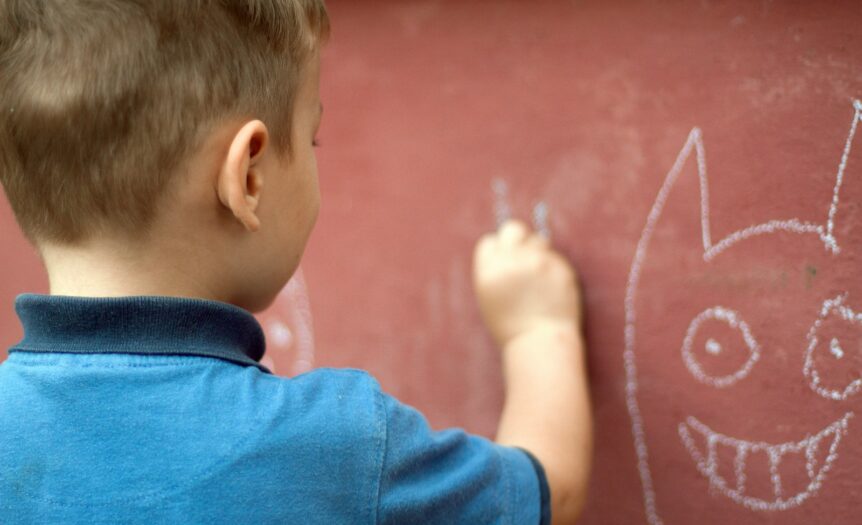 a little boy writing on a wall with a marker