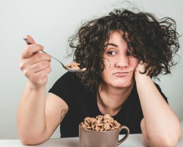 Διατροφή woman with messy hair wearing black crew-neck t-shirt holding spoon with cereals on top