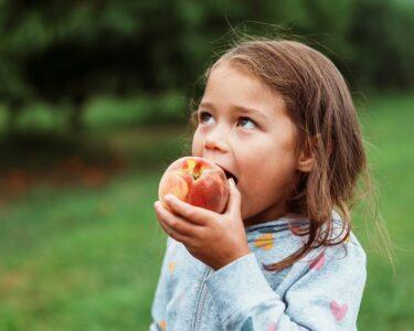 A young girl eating a fresh peach outdoors.