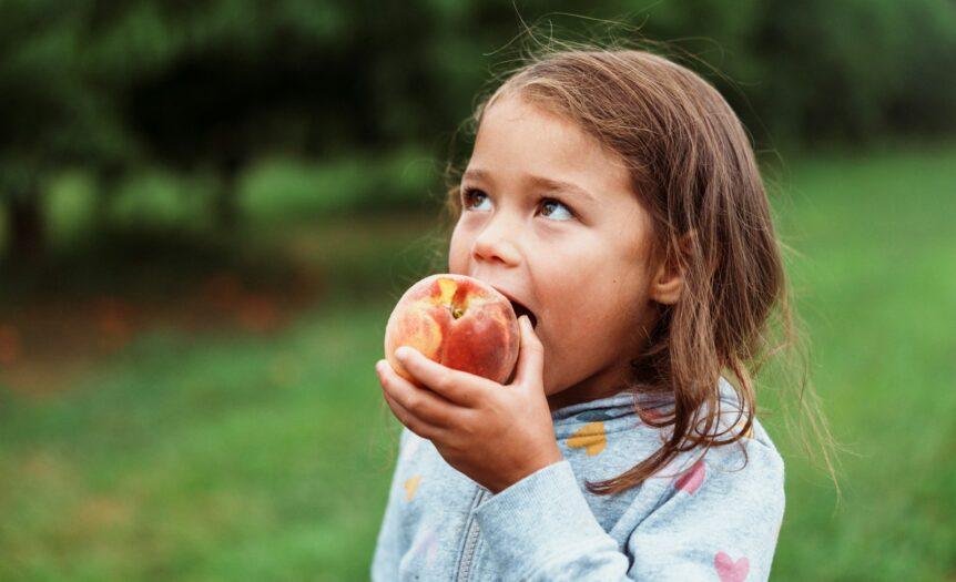 A young girl eating a fresh peach outdoors.