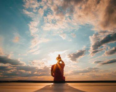 person sitting and facing back under blue and white sky