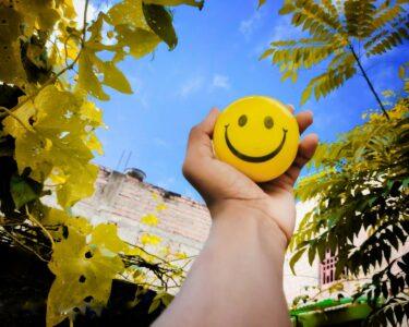 a hand holding a yellow smiley face ball