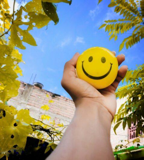 a hand holding a yellow smiley face ball