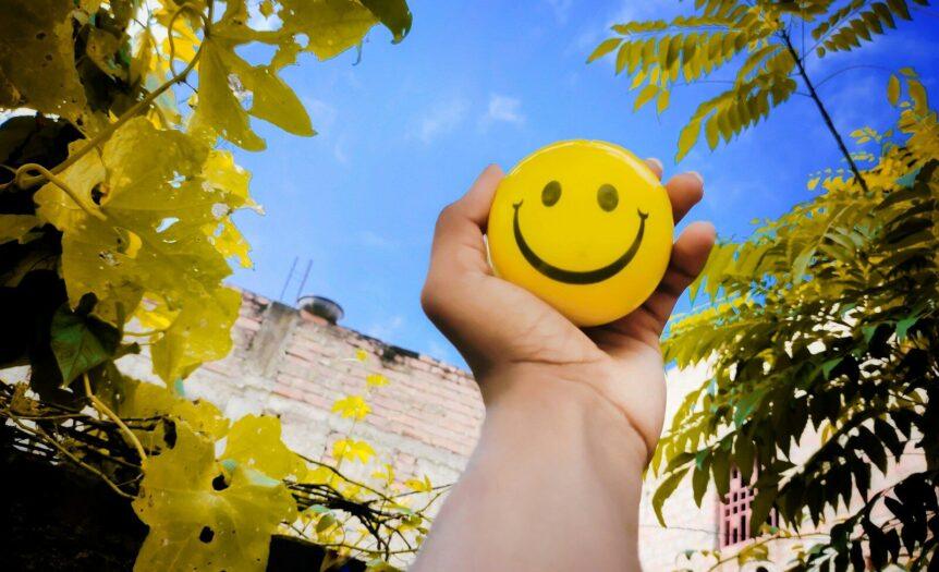 a hand holding a yellow smiley face ball