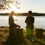 man in black jacket standing beside body of water during sunset