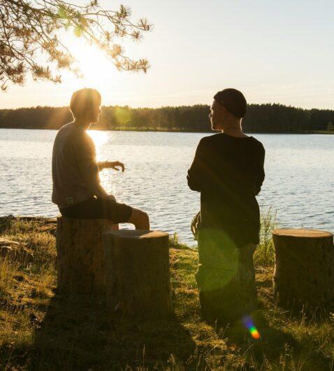 man in black jacket standing beside body of water during sunset