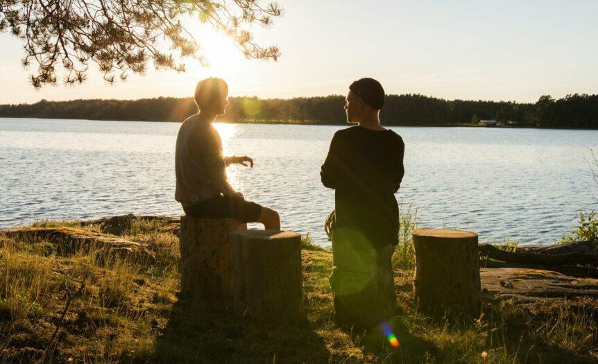 man in black jacket standing beside body of water during sunset