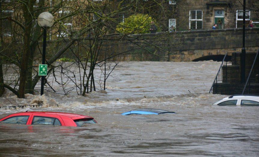 Three cars partially submerged in a flooded river near a stone bridge