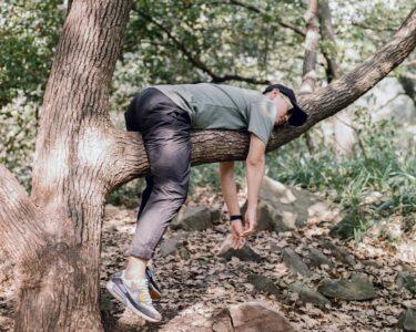 man in black t-shirt and blue denim jeans sitting on tree branch