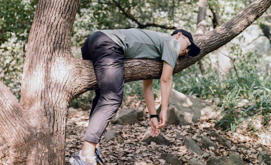 man in black t-shirt and blue denim jeans sitting on tree branch