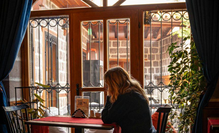 Γυναίκα κάθεται μόνη δίπλα σε παράθυρο σε ήσυχο χώρο — μοναξιά της Κυριακής