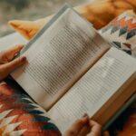 person reading book on brown and beige textile