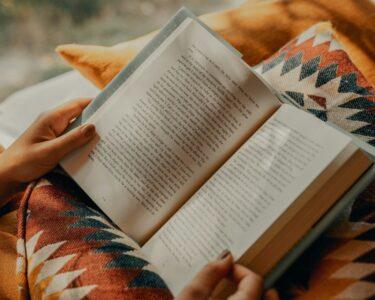 person reading book on brown and beige textile