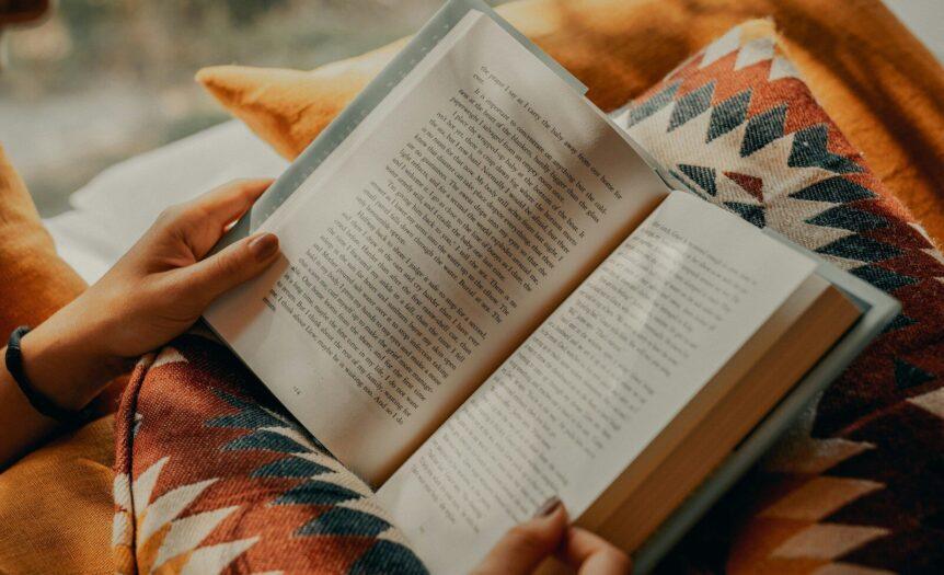 person reading book on brown and beige textile